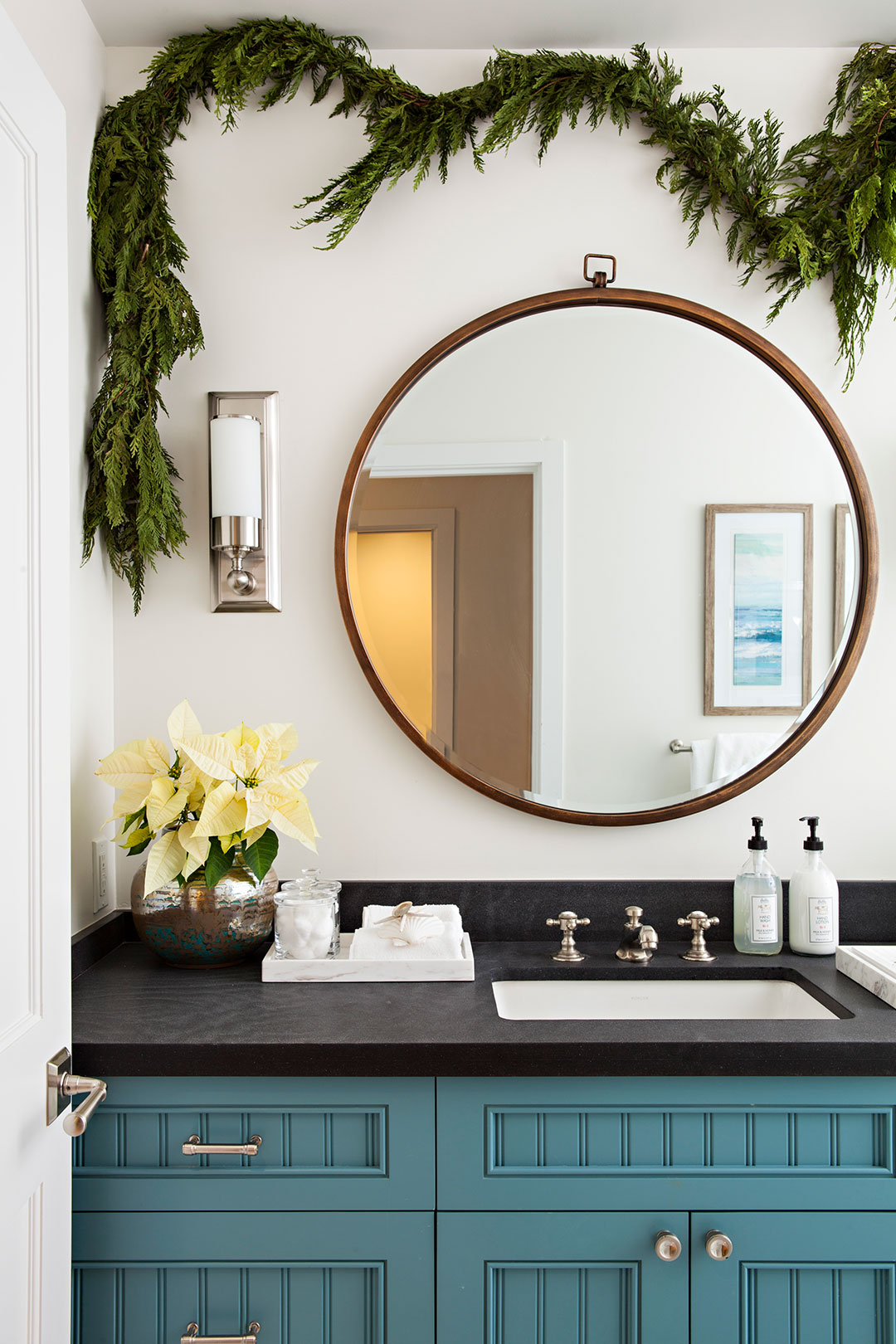 Natural greenery Christmas garland hung in the bathroom over a circular mirror.