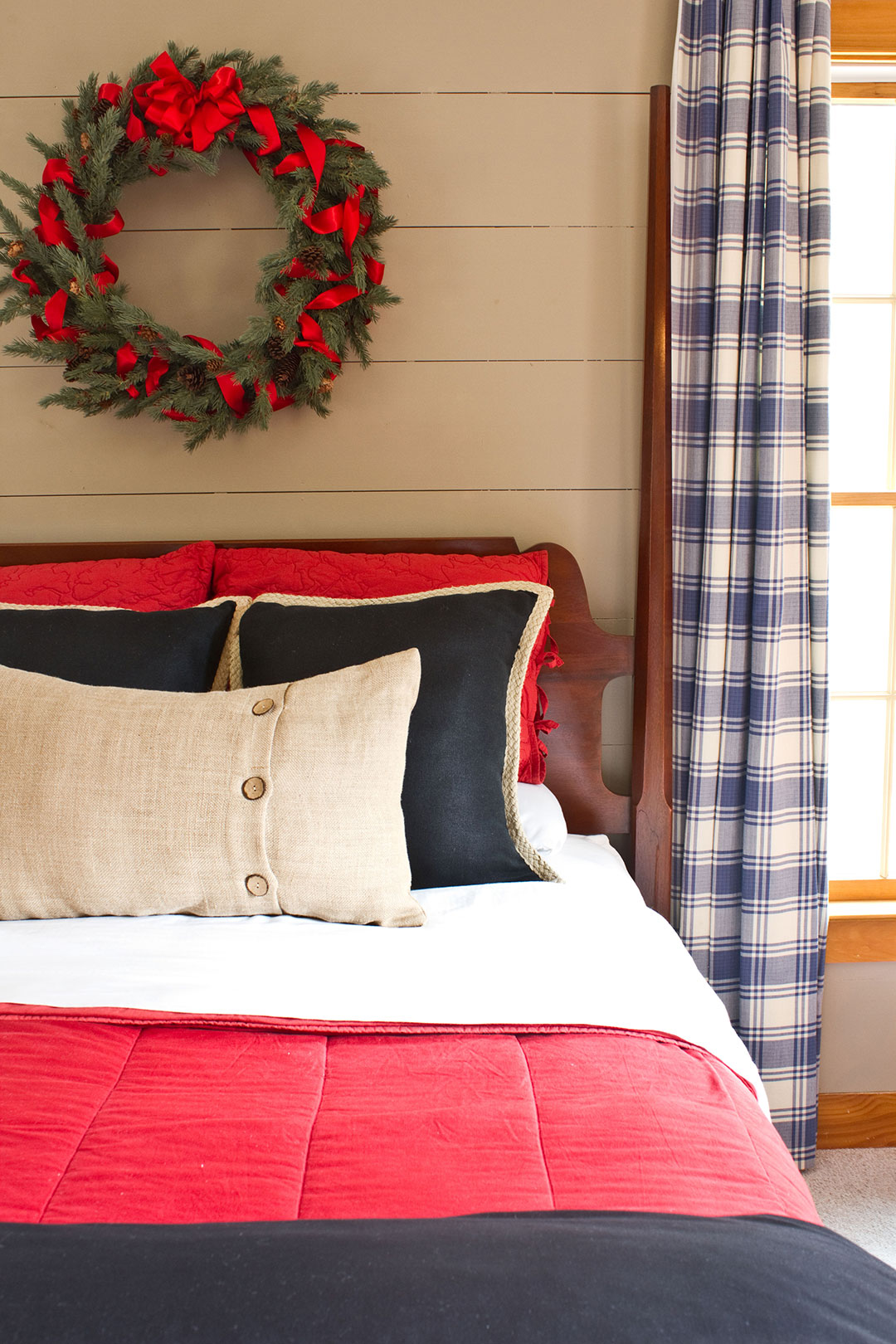 Gray shiplap wood paneled walls with wreath hanging over a guest bed for overnight holiday guests.