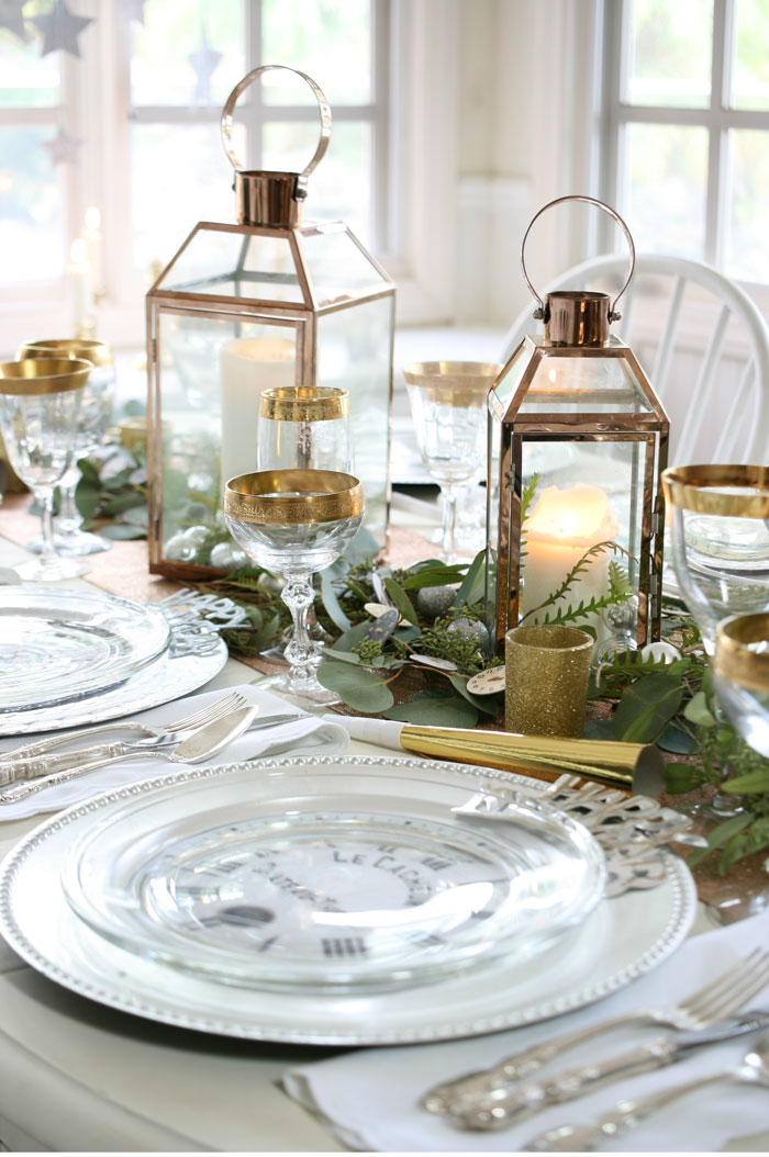 Copper lanterns, gold-rimmed champagne glasses, silver chargers and a rose gold table runner harmonize perfectly on this New Year’s Eve tablescape. 