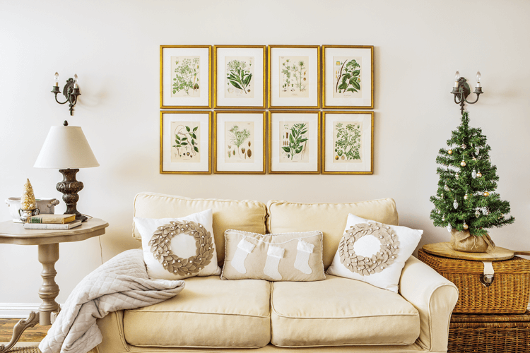 Vintage botanical prints hang over a love seat decorated with festive throw pillows