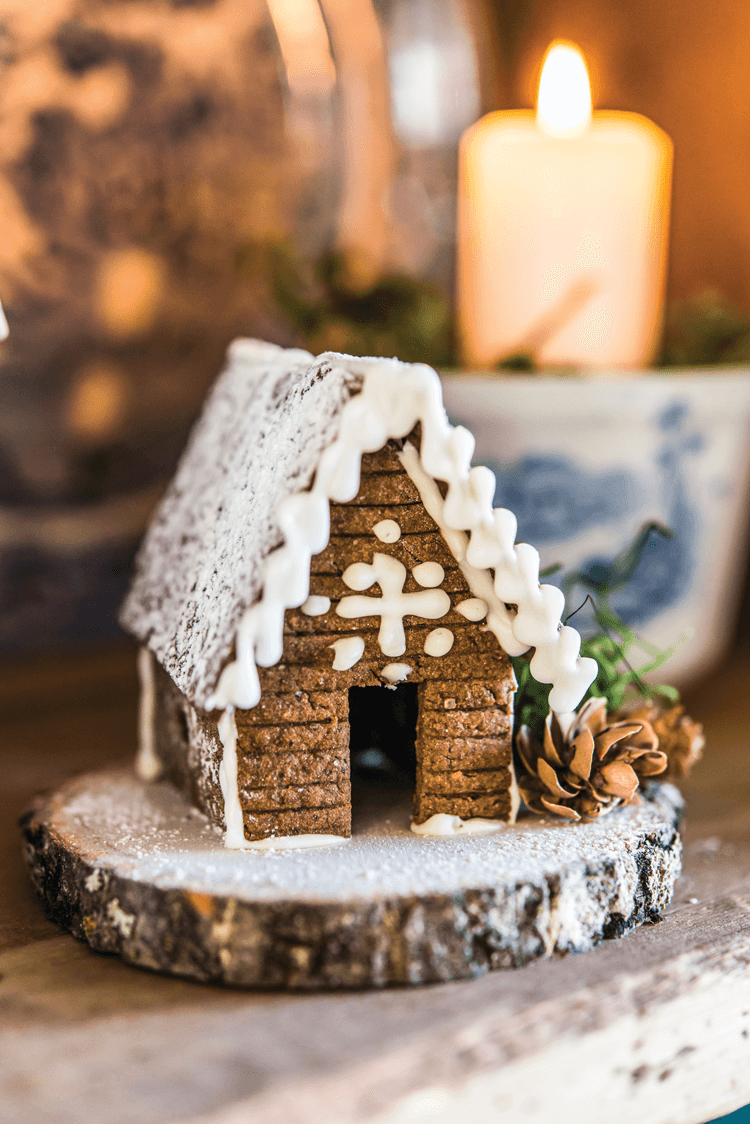 Small gingerbread cabin placed on a wooden stump. 