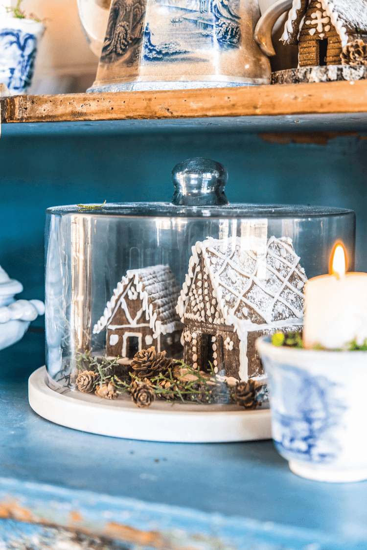 Small gingerbread village in display under a glass cake stand.