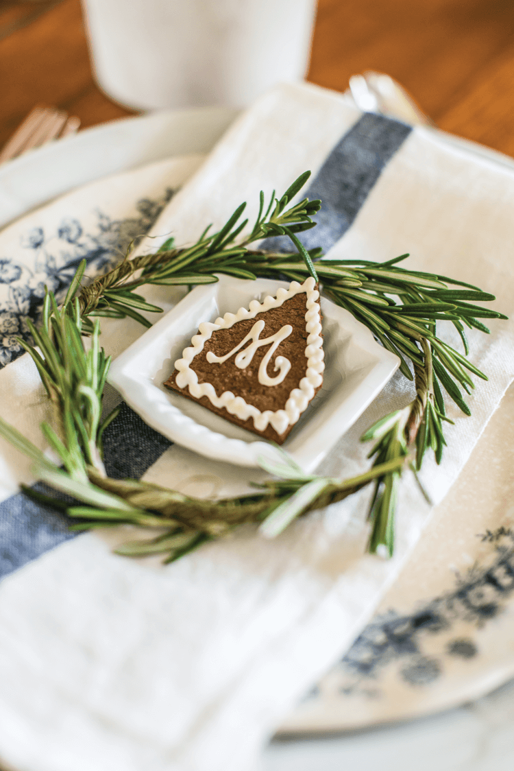 Place setting with white and blue china and a ring of greenery with a small monogrammed gingerbread cookie. 