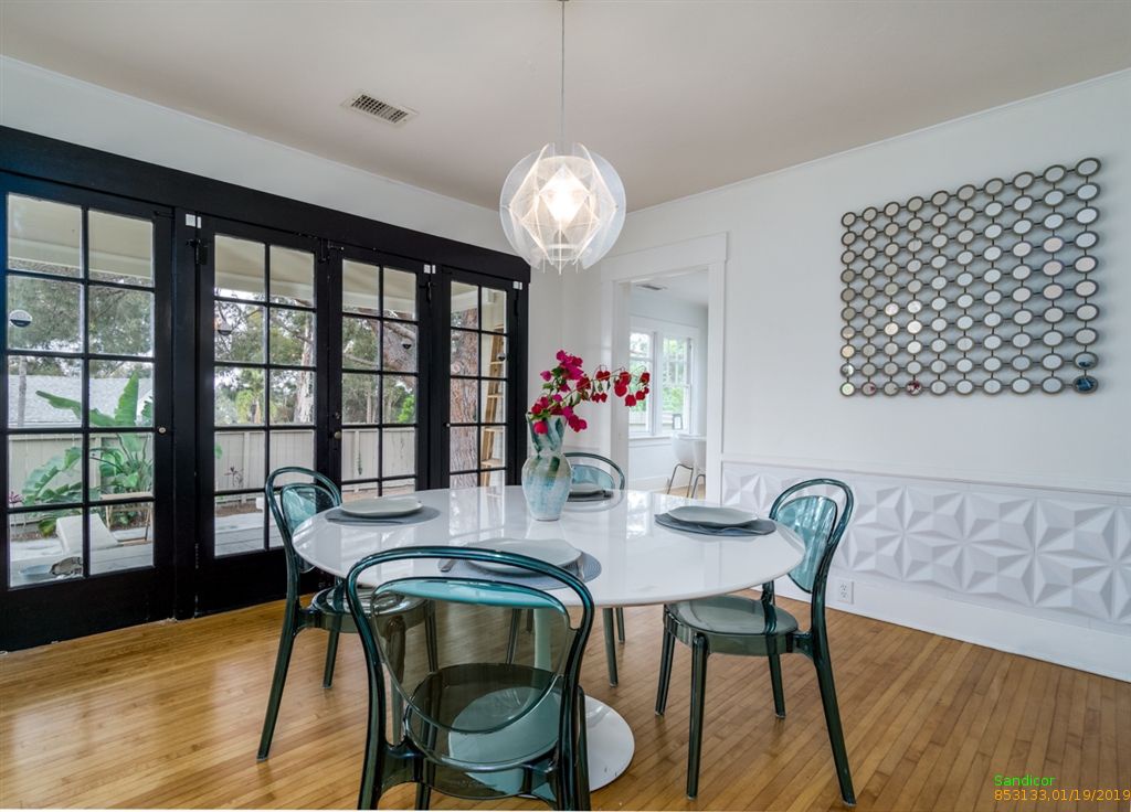 Trendy San Diego dining room with round white table, transparent turquoise chairs, and trendy chandelier.