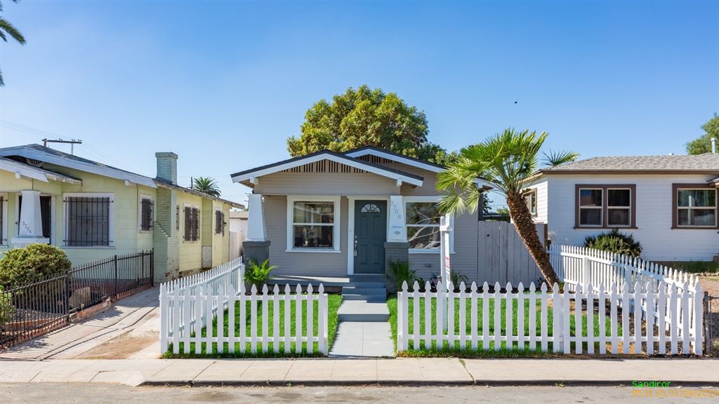 Adorable San Diego cottage with bright green front yard, white picket fencing, and slanted palm tree.