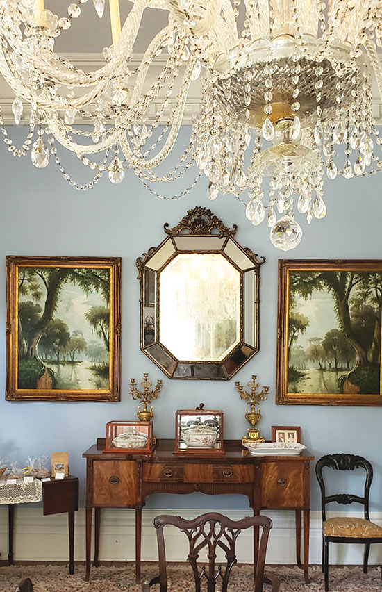 crystal chandelier above antique paintings and an elegant sideboard