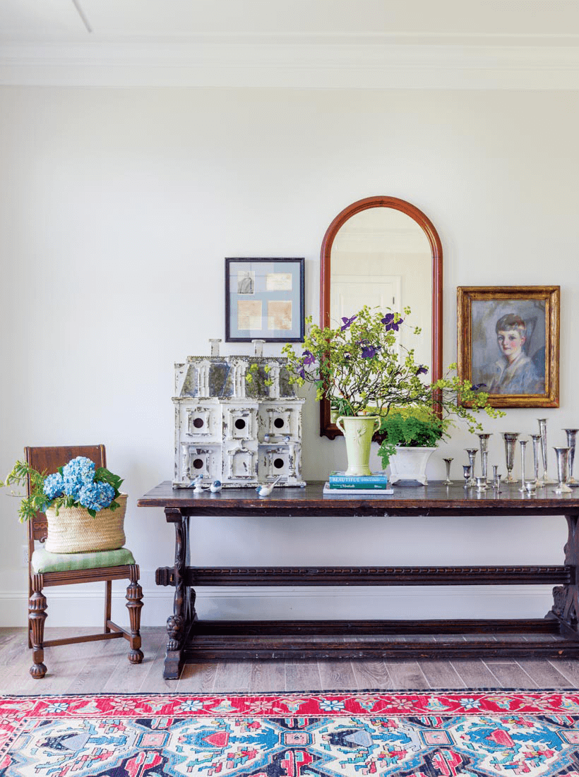 A dark wood table with an antique doll house and candlesticks.