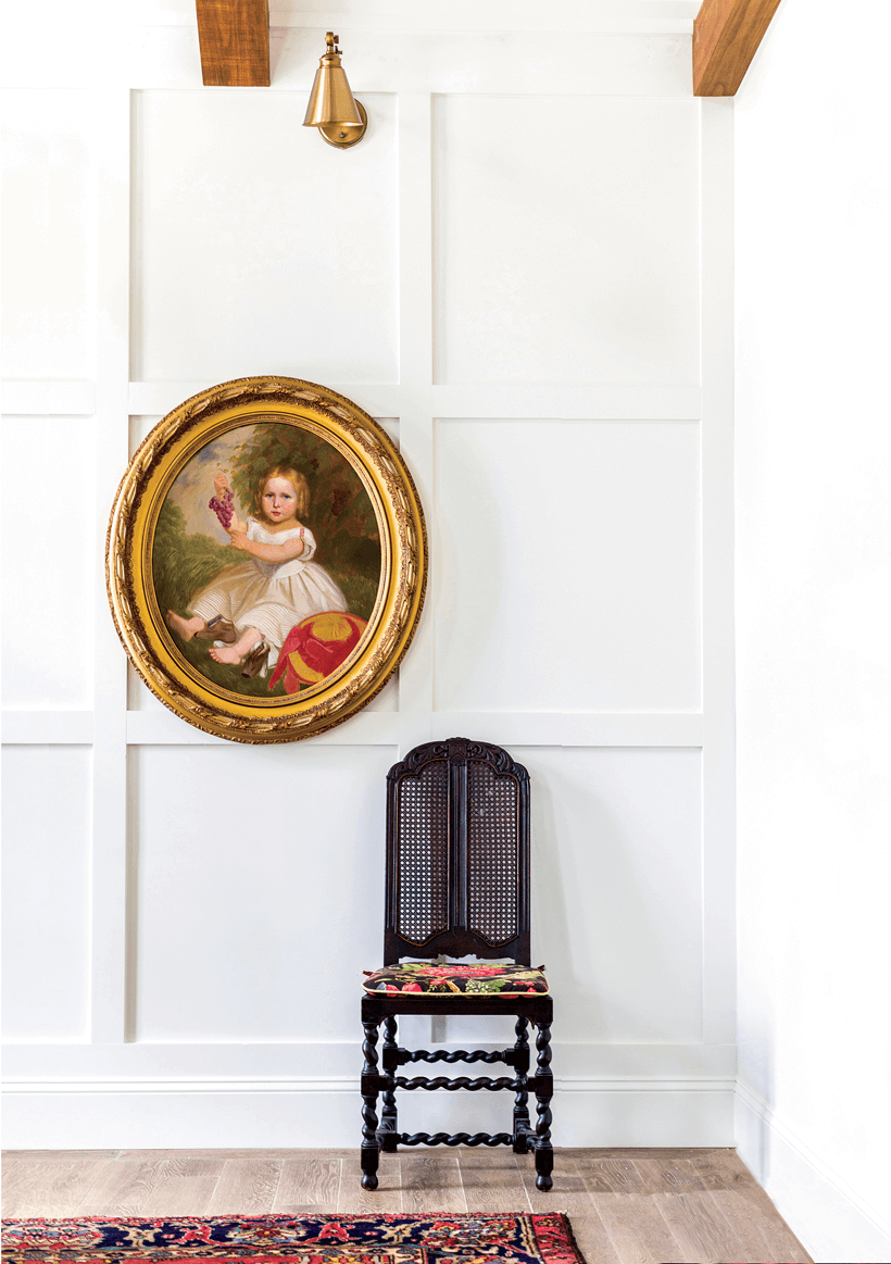 A gold-framed painting hung over a dark wooden chair, which contrasts with the white walls.