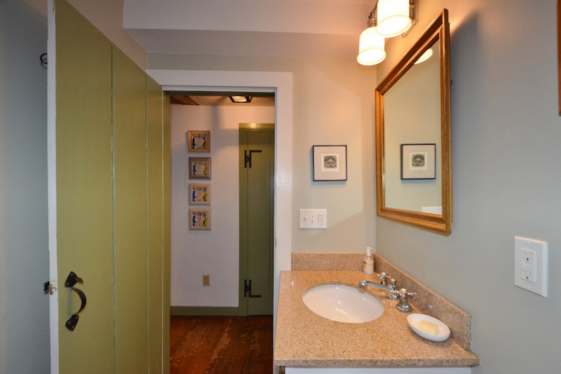 A bathroom with blue walls, one sink, and an old-fashioned green door.