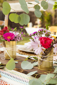 A table setting with gold-painted soup cans being used as vases.