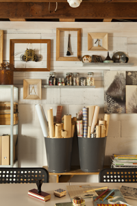 A craft room with open shelves and wooden picture frames. Two garbage cans are used to hold wrapping paper tubes.