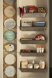 A wall with metal shelving on one side and on the other, paint can lids screwed into the wall are being used as small magnet boards.