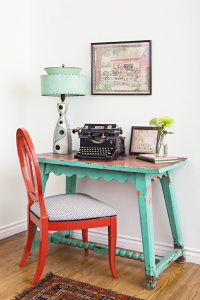 A small teal desk that's lightly distressed with a bright red chair.