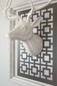 A black-and-white geometric pattern painted on a wall within a frame. A white ceramic deer is hung in the middle of the pattern.