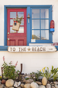A beach cottage with a red door and a blue door frame, as well as a blue window frame.
