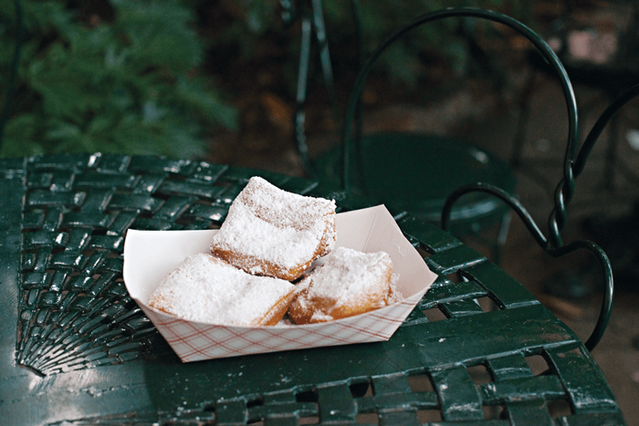 Three freshly sugar-dusted beignets displayed on an ornate, green metal chair. 