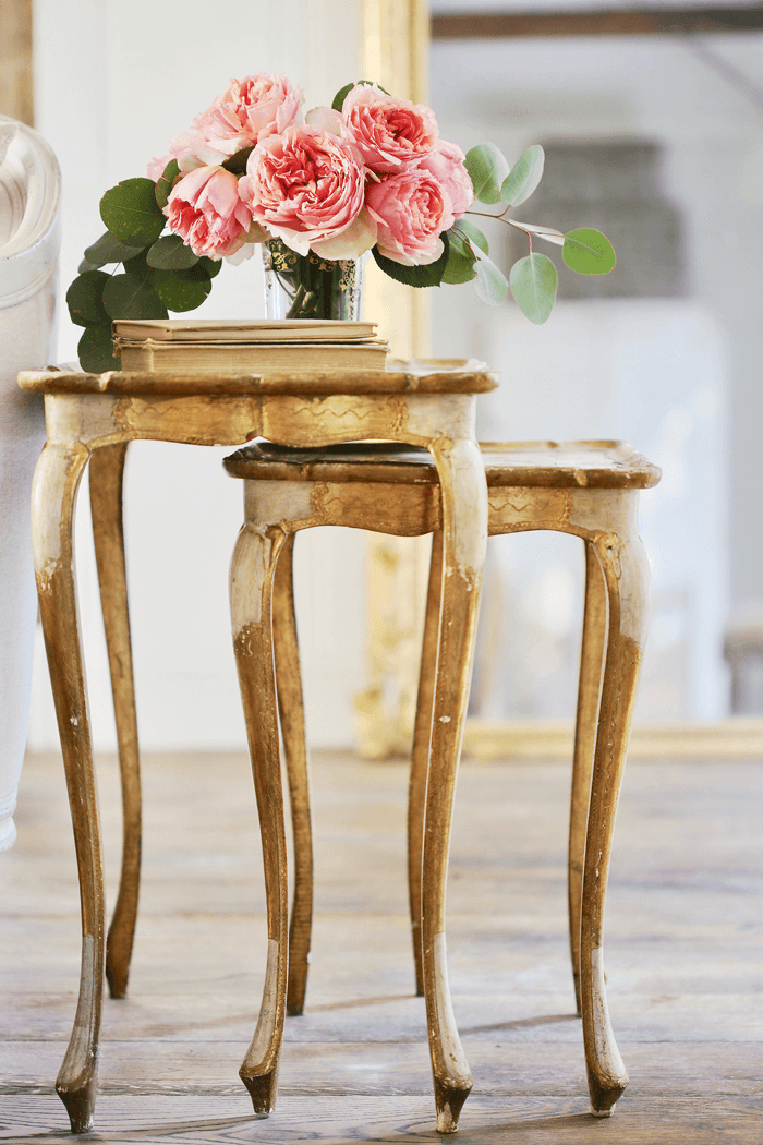 Vintage stacking console tables with a rustic gold finish topped with vintage books and fresh pink peonies. 