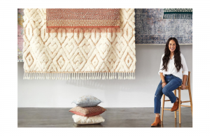 Joanna Gaines sitting on a stool, her new collection of rugs hanging behind her