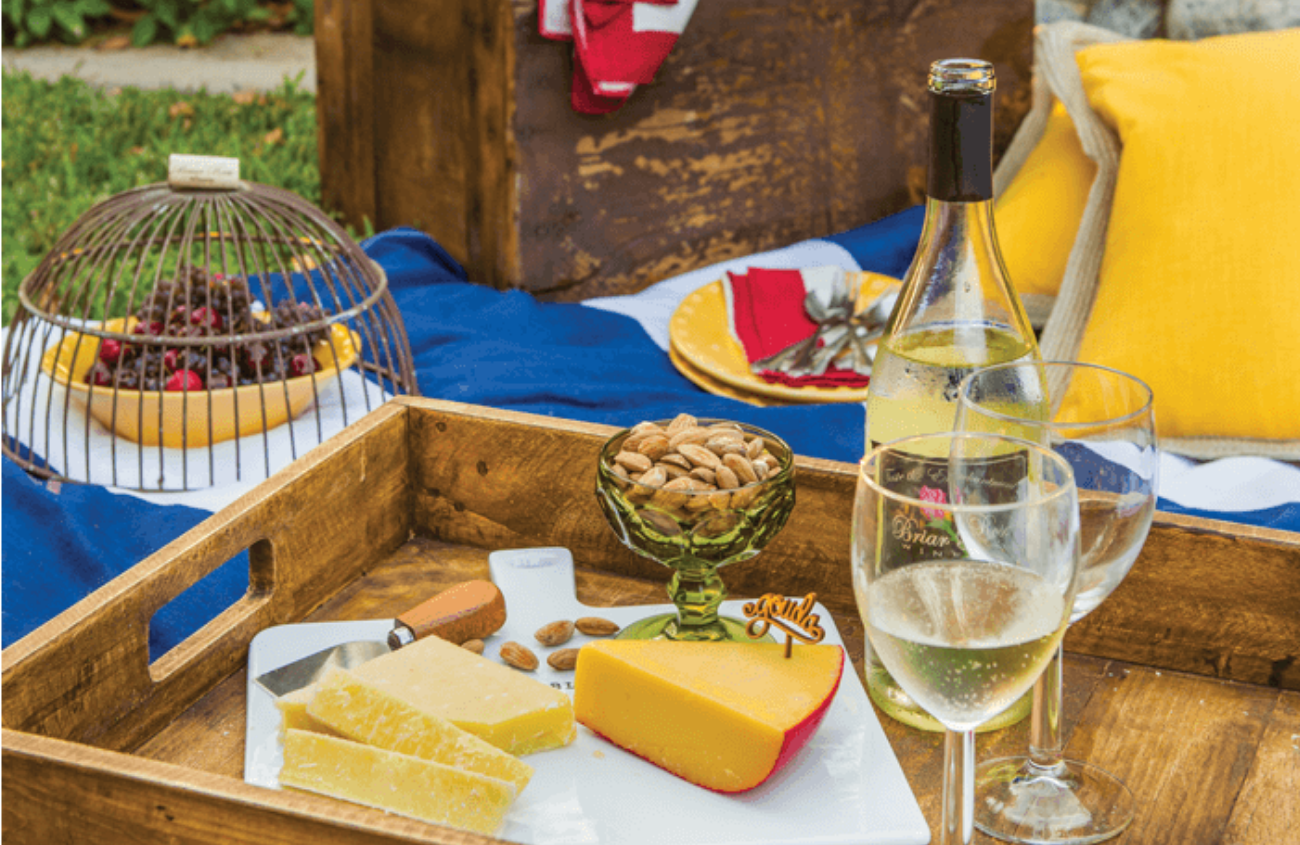Wine, cheese and appetizers set up as an outdoor picnic alongside a large basket
