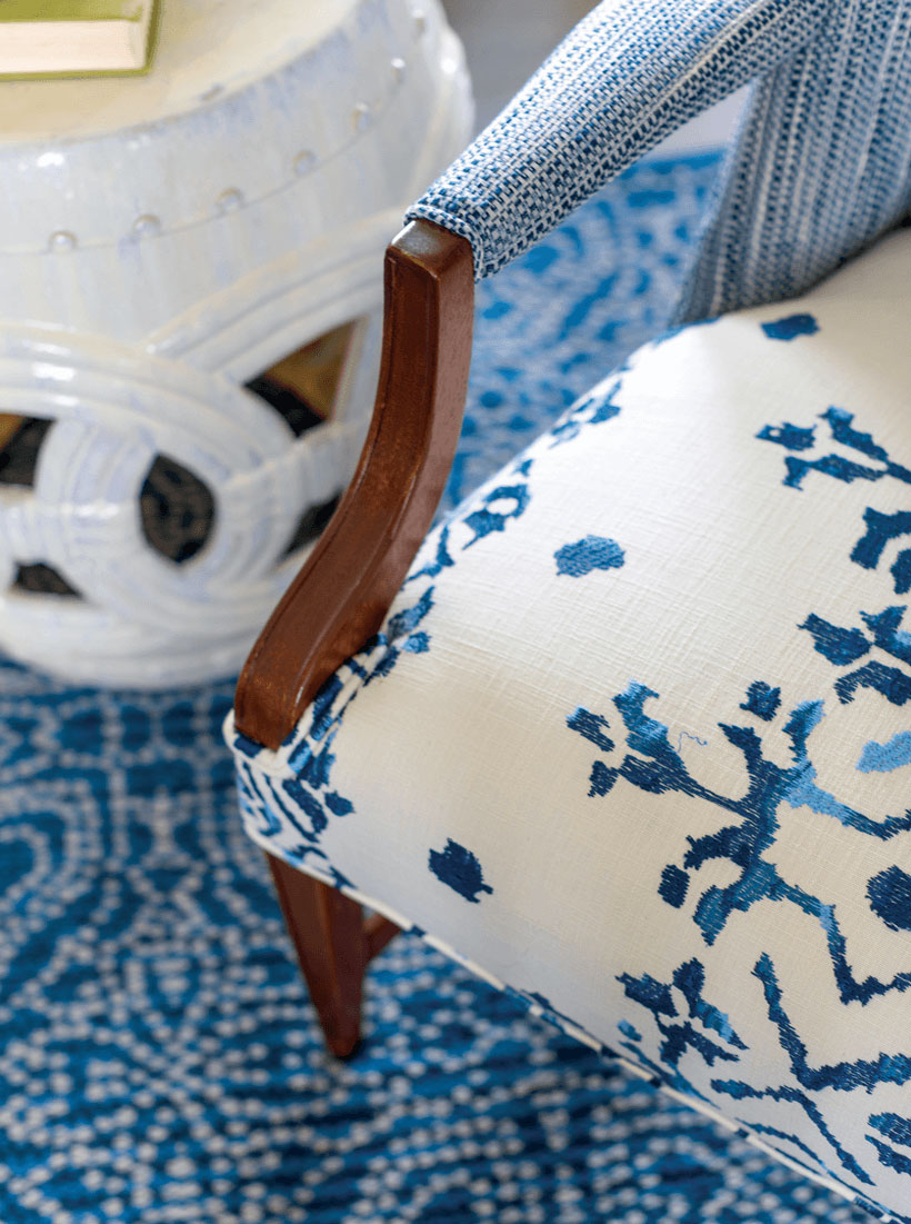 A white chair with blue accents and dark wooden arms and legs. The rug is also blue and white, and a small white end table is nearby.