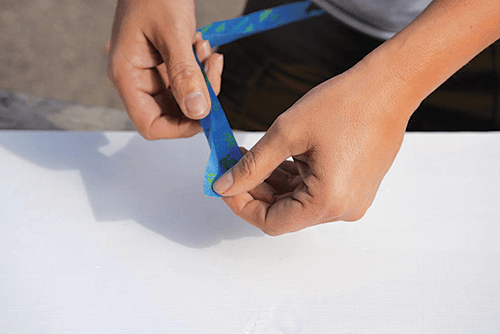 Hands holding painters tape over a white surface.