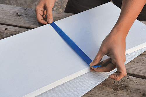 Hands placing painters tape in the center of a white tray. 