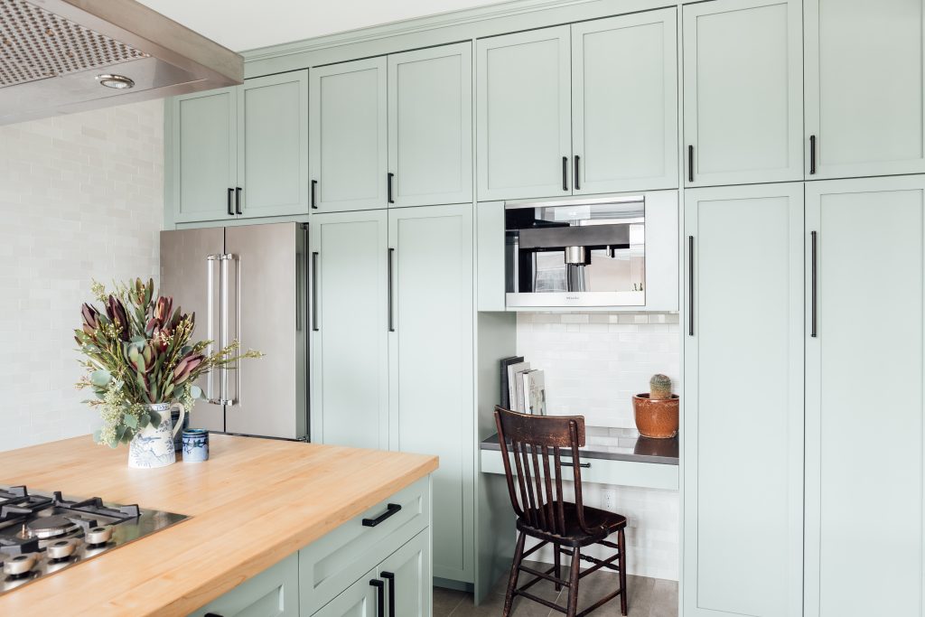 a wall of sea-green cabinets with a built-in desk nook