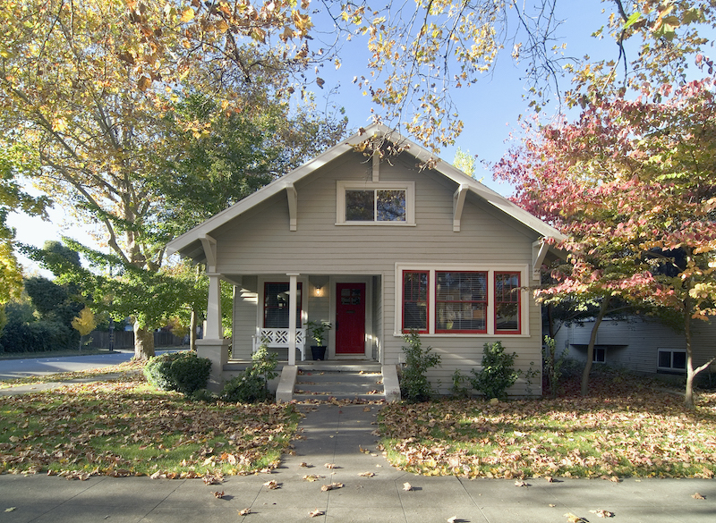 Front exterior of a gray bungalow with red door