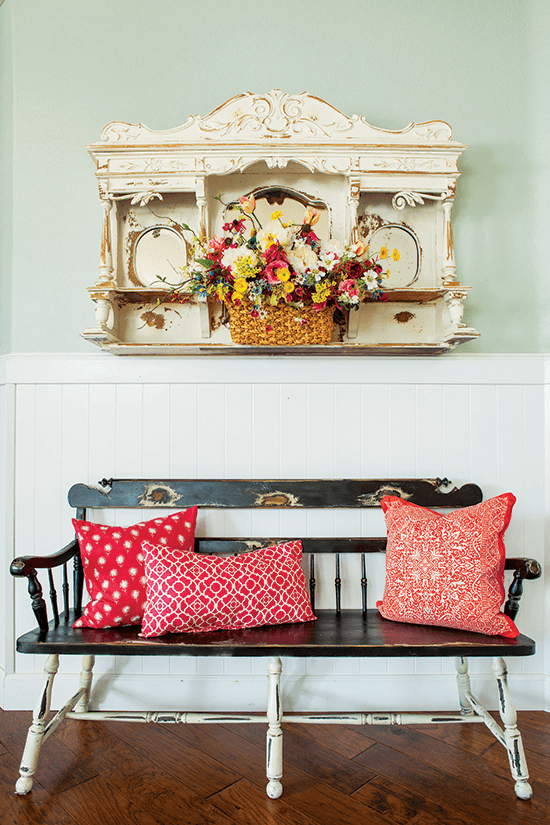 Found and repurposed vintage bench in an entryway, decorated with bright red pillows. 