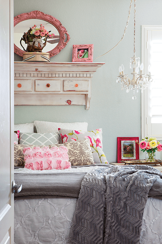 Warm and cozy bed with fuzzy gray throw at the end of the bed. Pink accents and a lovely statement piece above the bed with a small crystal chandelier hanging over the bedside table. 