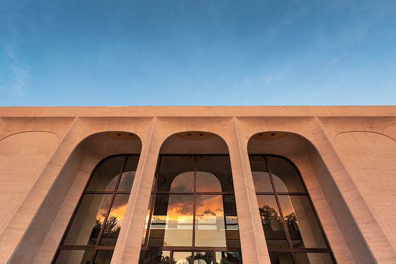 An exterior image of a building with large archways during sunset.