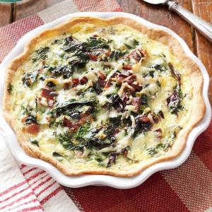 A quiche with bacon and spinach cooked on top.
