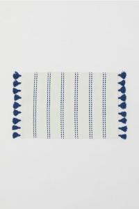 A white bath mat with blue stripes and blue tassels.