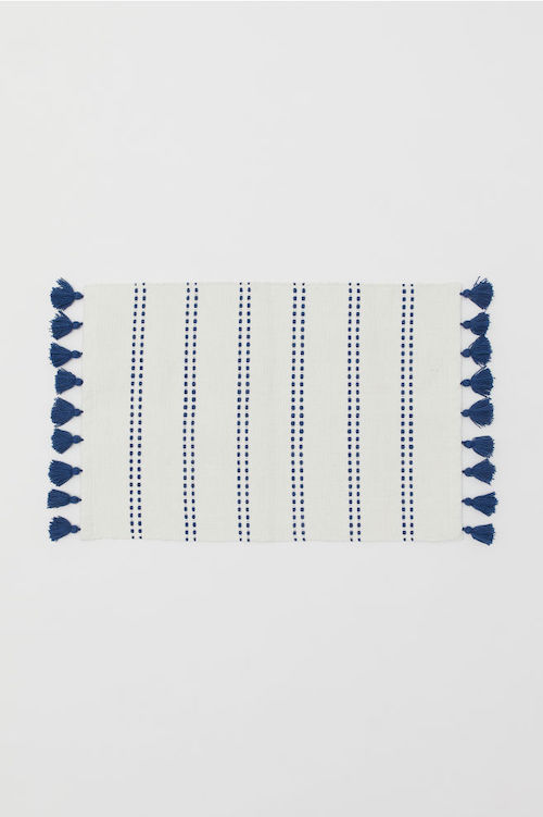 A white bath mat with blue stripes and blue tassels.