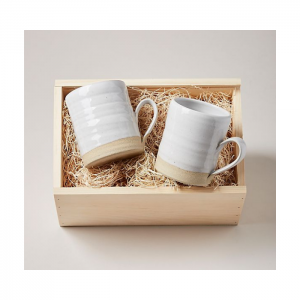 Two simple pottery mugs, white, glaze finish arranged in a wooden box for display.