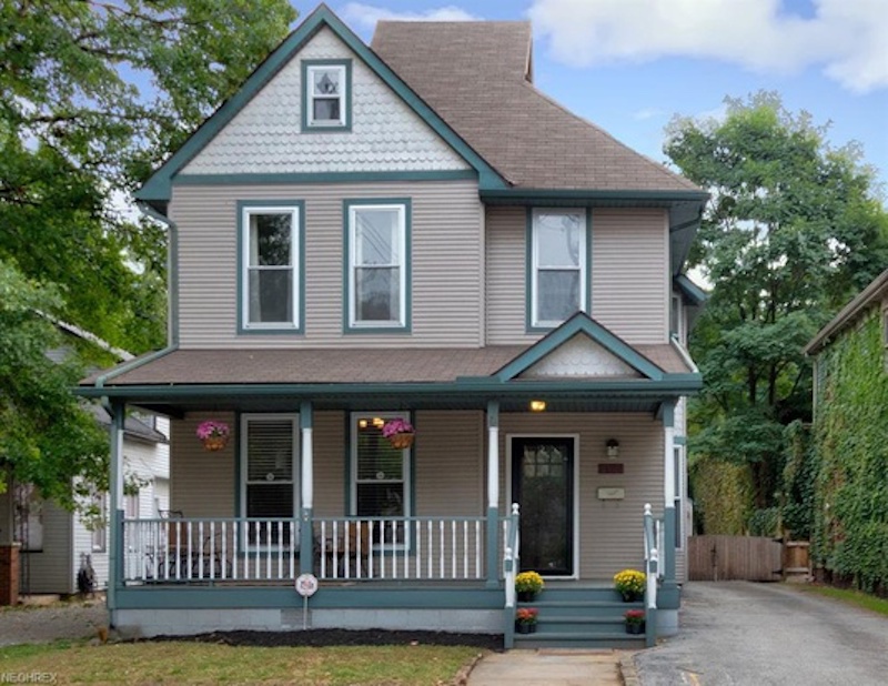 A blue and grey cottage with flowers and a porch.