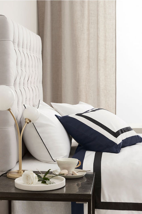 A bed with a white bedspread with dark blue edges.