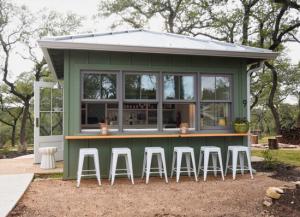 Outdoor bar top and stools lined up under a pass through window.