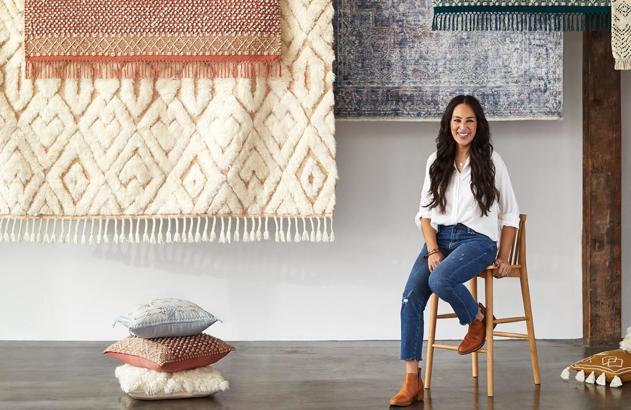 Joanna Gaines sitting in front of a display of her new line of rugs
