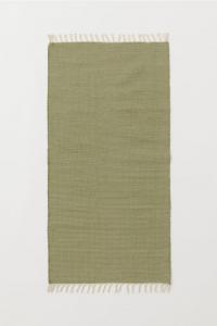A khaki green rug with fringe on the short ends.