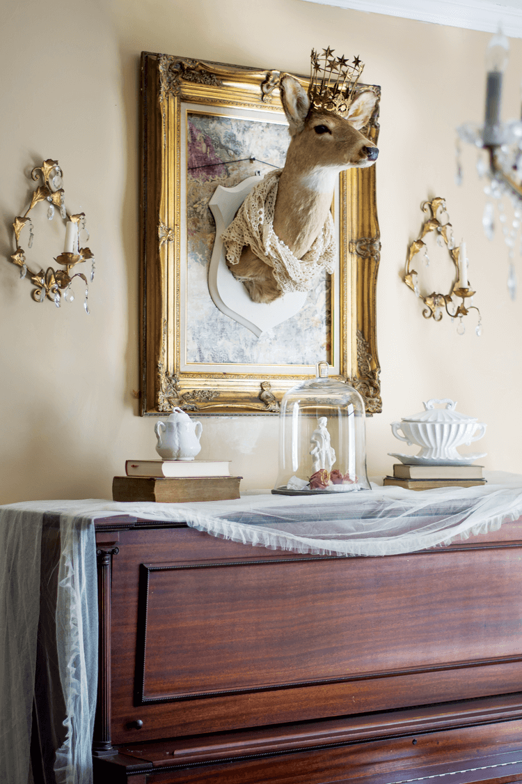 deer head framed in a vintage gold frame and mounted on a wall above a piano. 