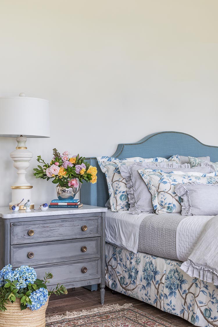 A blue bed with floral pattern linens and a gray nightstand