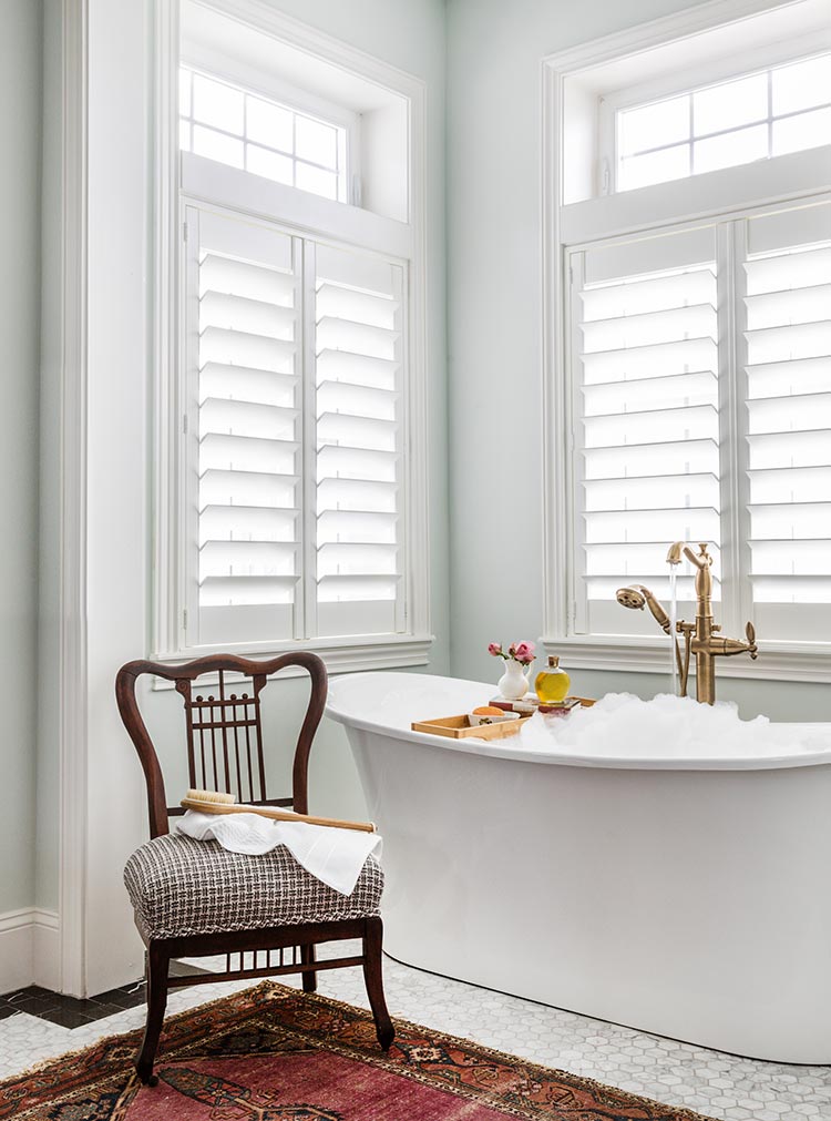 This bathroom has trendy marble floor tiles and a modern bathtub with an antique rug and vintage-inspired faucets.