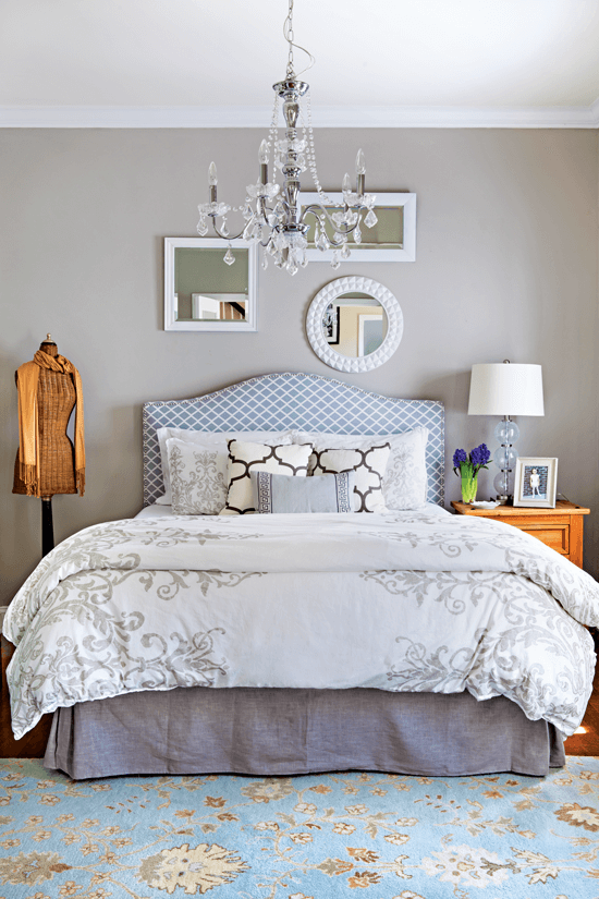 Light and bright bedroom with glossy white painted frames decorating the wall behind the headboard, with a wooden vintage dress from next to the bed. 