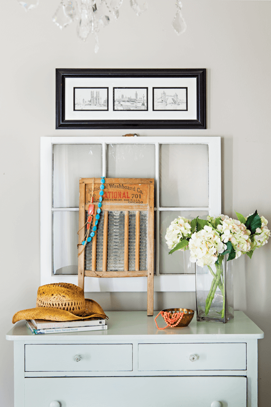 Light colored dresser against a white wall. stopped with a vase of white hydrangeas, an old window and washboard and a straw hat on top.