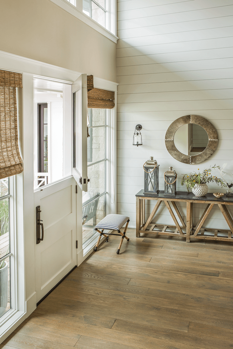 well lit rustic beach farmhouse entryway featuring a double hung door circle mirror and console along a white shiplap wall