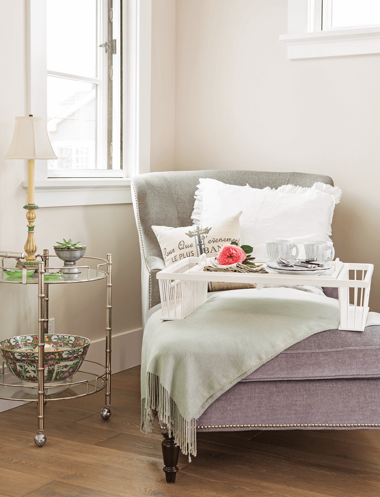 bright nook lit by window light featuring a gray chaise draped with a cozy blanket and topped tea set on a tray