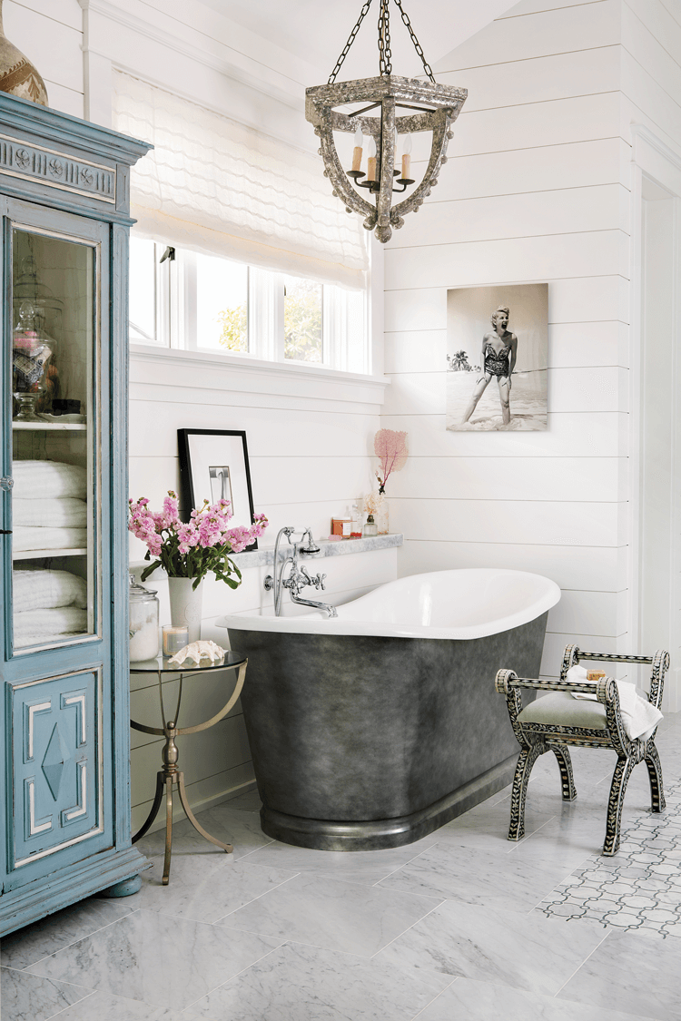 white bathroom featuring a cast iron bath tub white shiplap walls marble floors and chandelier with metal finish
