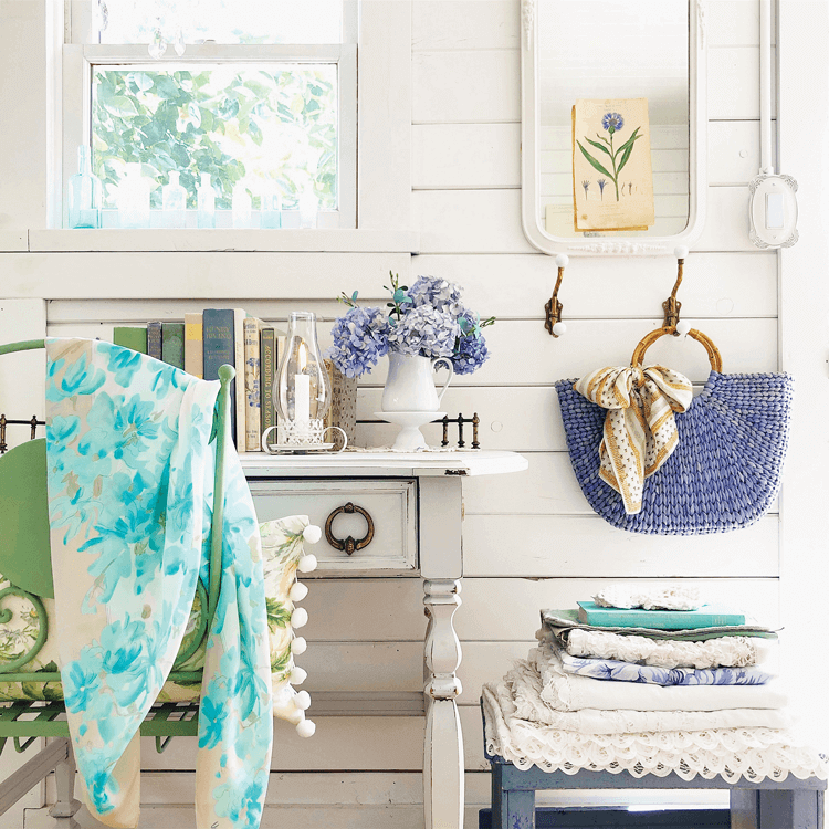 a white cottage writing desk against a shiplap wall, pretty blue linens in a stack