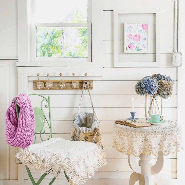 a small tea table with a lace doily, a green metal garden chair and wall hooks